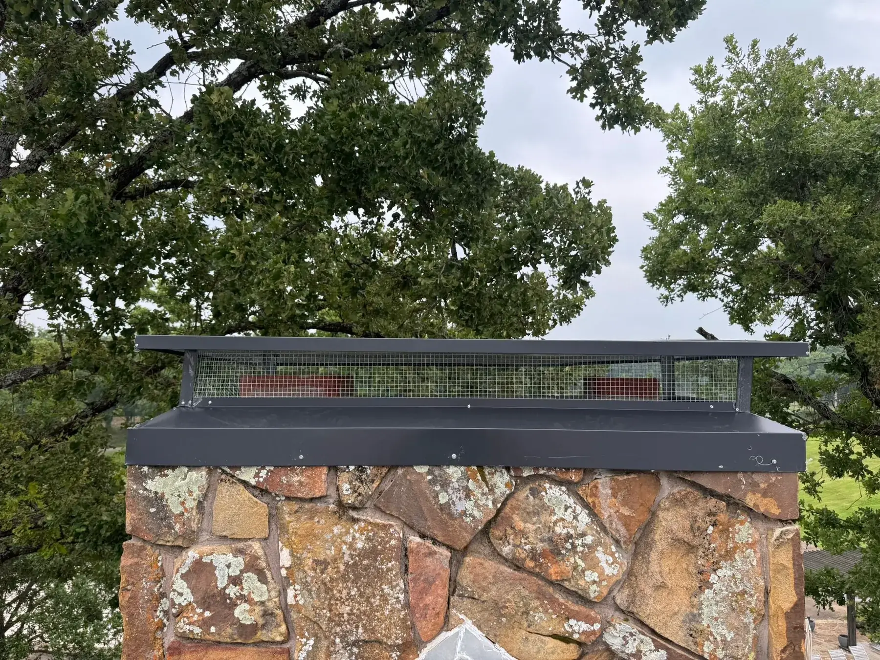 Stone chimney fitted with a new custom cap on a completed Chimney Standard job